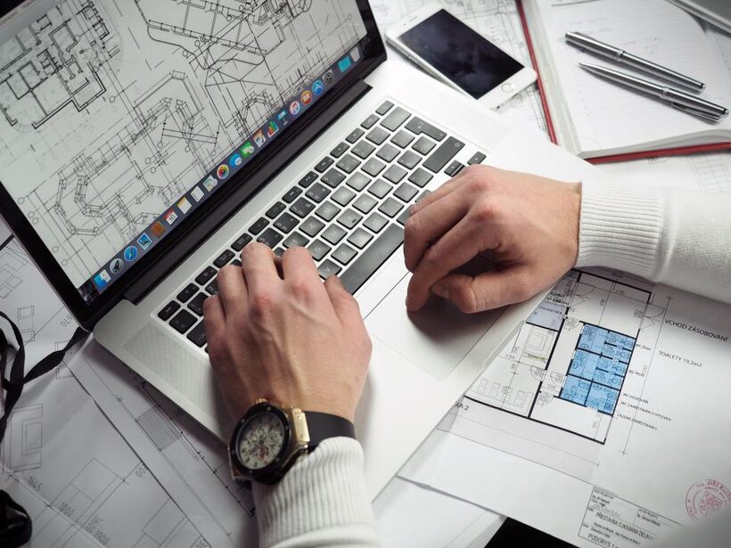 An architect's desk with blueprints and a laptop showing a website layout