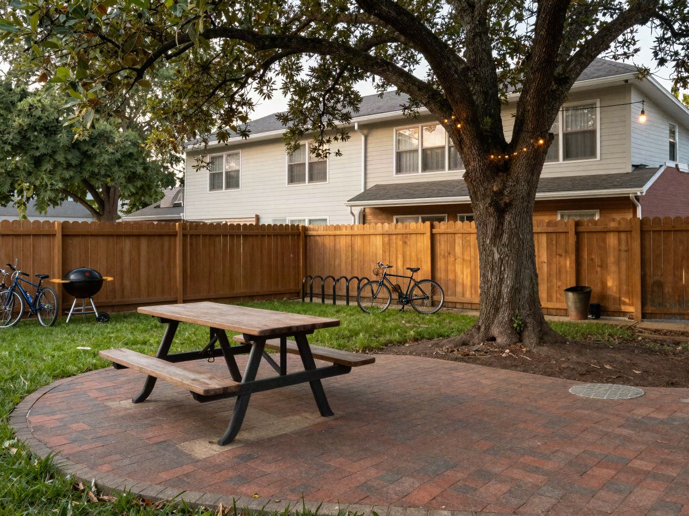 The fenced backyard with a brick patio, a picnic table and string lights